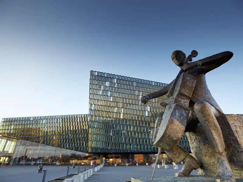 Bronzestatue eines Cellisten vor der beeindruckenden Glasfassade des Konzerthauses Harpa in Reykjavik, ein Highlight jeder Gruppenreise nach Island