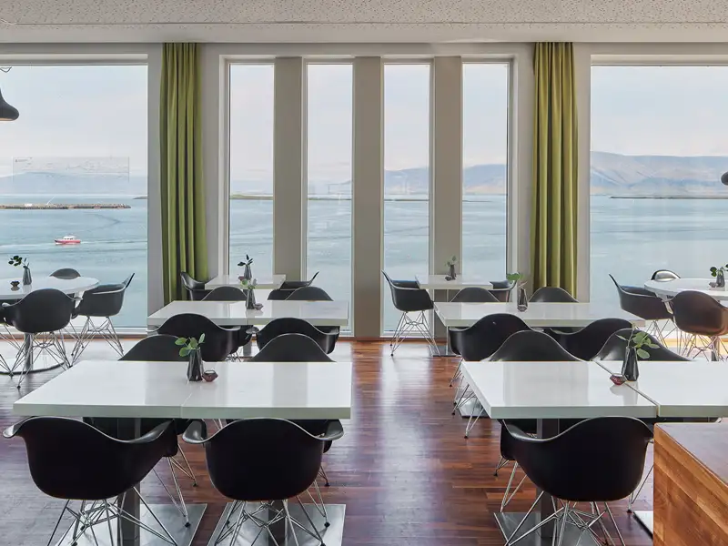 Moderner Hotel-Speisesaal in Island mit Panoramablick durch große Fenster auf eine Bucht und die Berge bei Reykjavik.