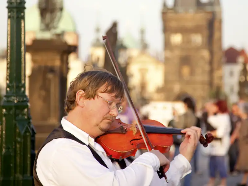 Ein Straßenmusiker spielt Geige auf der Karlsbrücke, ein typisches Erlebnis während der Stadterkundung in Prag.