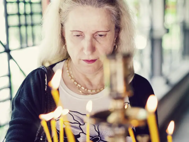 Eine Person blickt auf die Flammen von Kerzen vor einer orthodoxen Kirche,