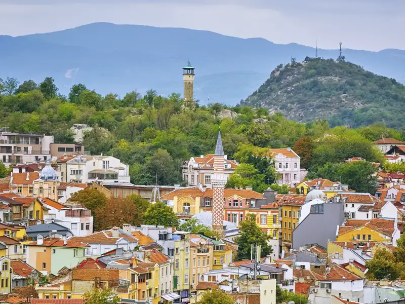 Blick über die Altstadt von Plovdiv während eines Stadtrundgangs, mit traditionellen Häusern,dem Minarett der Dschumaja-Moschee und einem der charakteristischen grünen Hügel der Stadt im Hintergrund.