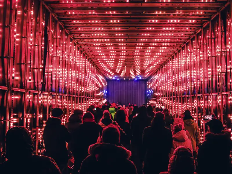 Eine Reisegruppe, von hinten gesehen, durchquert eine Lichtinstallation in einem Tunnel mit roten Lichtern. Ein Beispiel einers der Kunstwerke des Vilnius-Light-Festivals, dessen Besuch als Leistung dieser Reise inkludiert ist.