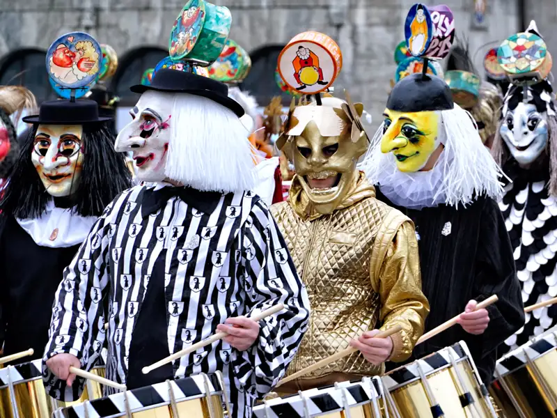 Eine Gruppe maskierter Tambouren in Kostümen trommelt während der Basler Fasnacht, einem zentralen Erlebnis dieser Eventreise mit Studiosus in die Schweiz.