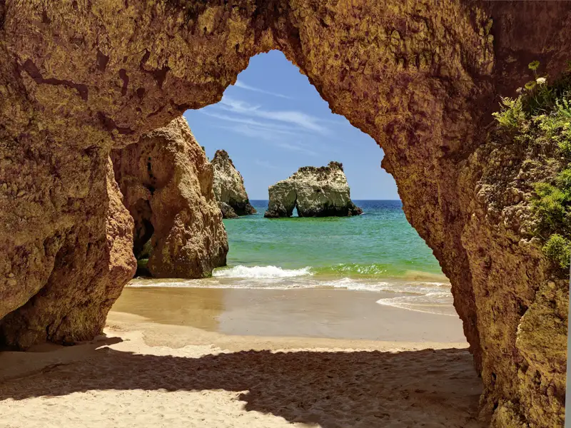 Auf unserer Gruppenreise mit Studiosus werfen wir einen Blick durch ein Felsentor auf den Atlantik an der Algarve, eine Felsformation am Praia dos Três Irmãos, einem  malerischem Strandabschnitt im Osten von Alvor, Algarve, Portugal.