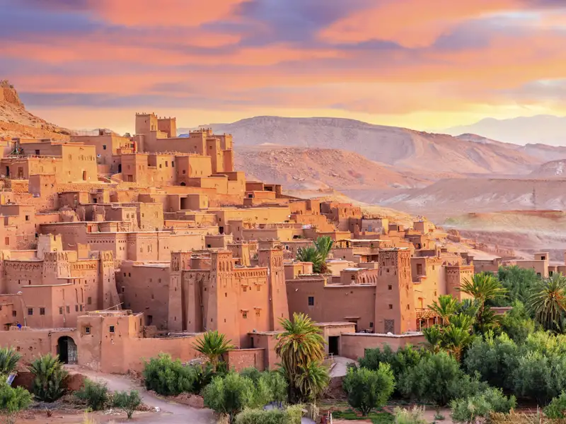 Auf unserer Gruppenreise mit Studiosus besuchen wir die Lehmfestung Aït-Ben-Haddou, UNESCO-Weltkulturerbe, bei malerischem Sonnenuntergang während einer Marokko-Rundreise.