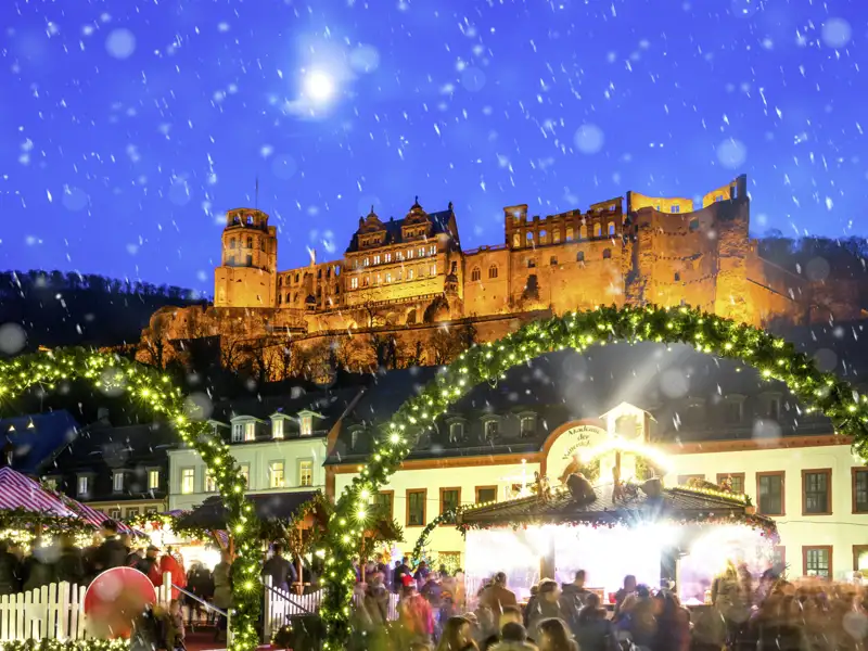 Auf unserer Silvesterreise besuchen wir den Weihnachtsmarkt in Heidelberg mit Buden und Lichtern vor der beleuchteten Burg im Schnee.