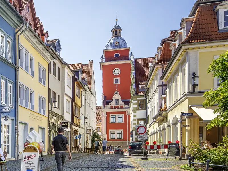 Auf unserer Gruppenreise mit Studiosus genießen wir den Blick durch eine Gasse mit bunten Häusern auf das Alte Rathaus in Gotha, ein Highlight während des Stadtrundgangs im Rahmen der Städteeise.