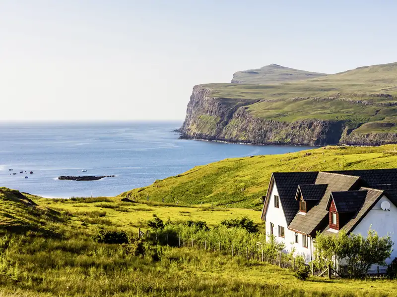 Auf unserer Gruppenreise mit Studiosus genießen wir den Ausblick auf ein typisches Haus an der Küste der Isle of Skye, umgeben von grünen Hügeln und dem Meer. Ein Natur Highlight auf unserer Kreuzfahrt durch Schottland.