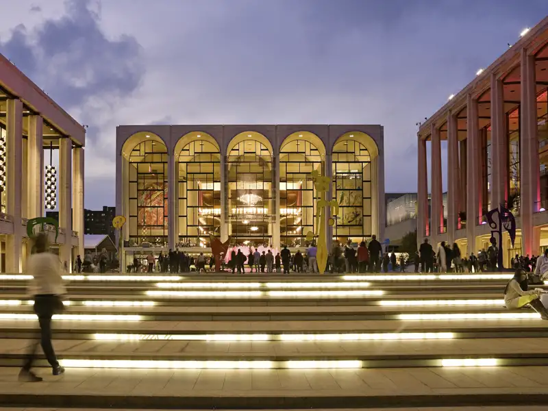 Auf unserer Gruppenreise nach New York bewundern wir die beleuchtete Fassade der Metropolitan Opera bei Dämmerung. Dies ist immer ein Highlight unserer Rundreise nach New York.