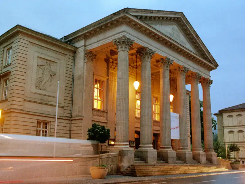 Auf unserer Gruppenreise mit Studiosus bewundern wir die Außenansicht eines neoklassizistischen Theaters in Meiningen mit Säulengang am Abend. Das prachtvolle Gebäude ist ein Highlight jeder Städtereise.