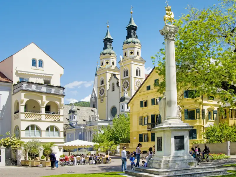Der barocke Brixner Dom an einem sonnigen Tag, gesehen vom belebten Domplatz mit seinen Cafés und historischen Gebäuden, ein toller Ausblick auf unserer Studiosus Gruppenreise.