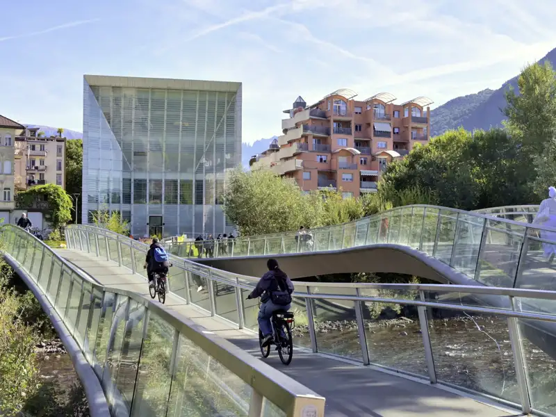 Zwei Radfahrer auf einer geschwungenen Brücke über die Talfer in Bozen, im Hintergrund das Museum Museion, ein toller Stopp auf unserer Rundreise mit Studiosus.