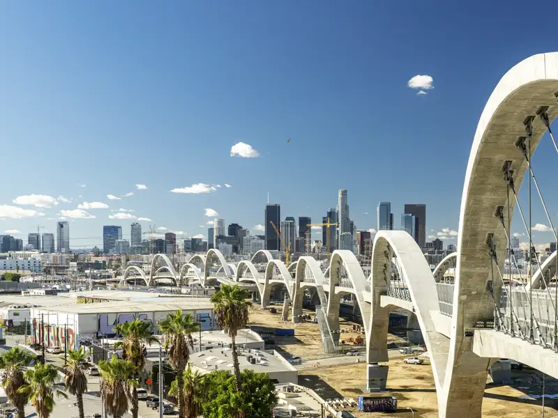 Die markante Bogenarchitektur der Sixth Street Viaduct vor der sonnigen Skyline von Downtown Los Angeles mit Palmen, ein toller Anblick auf unserer Rundreise mit Studiosus.