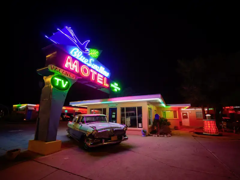 Ikonisches Neon-Schild des Blue Swallow Motels an der Route 66 in Tucumcari erhellt nachts einen Oldtimer, ein Highlight unserer Gruppenreise mit Studiosus.