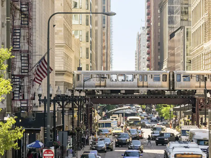 Die ikonische Hochbahn 'The L' in Chicago fährt über eine Brücke in einer belebten Straßenschlucht mit viel Verkehr, ein toller Anblick auf unserer Studiosus Rundreise durch die USA.