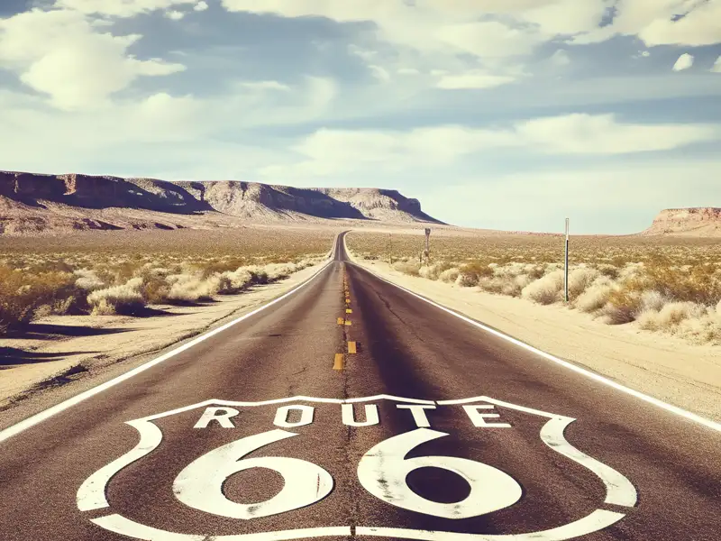Das ikonische Route 66 Schild auf dem Asphalt einer Straße, die auf einer Studienreise endlos durch die Wüste Arizonas führt.