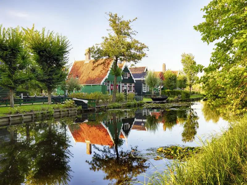 Die typisch holländischen, grünen Holzhäuser einer idyllischen Ortschaft spiegeln sich im ruhigen Wasser eines Kanals, ein toller Ausblick auf unserer Gruppenreise mit Studiosus.