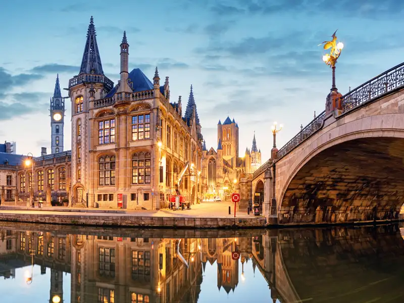 Abenddämmerung in Gent: Die beleuchteten Gildehäuser am Graslei spiegeln sich im Wasser der Leie neben der St.-Michaels-Brücke, ein Highlight unserer Studiosus Gruppenreise nach Belgien.