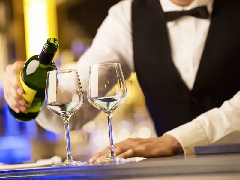 Kellner mit Weste und Fliege serviert bei einer Weinprobe auf einer Studienreise im Baskenland spritzigen Txakoli-Weißwein.