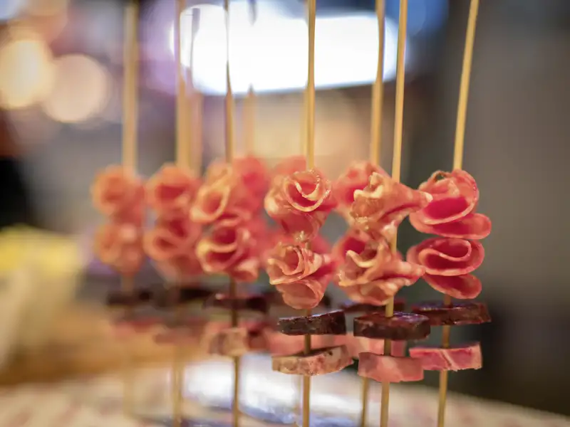 Nahaufnahme von kunstvoll zubereiteten Pintxos im Baskenland: Holzspieße mit Rosen aus Schinken und Wurststückchen, ein kulinarische Highlight auf unserer Kulturreise mit Studiosus nach Barcelona.