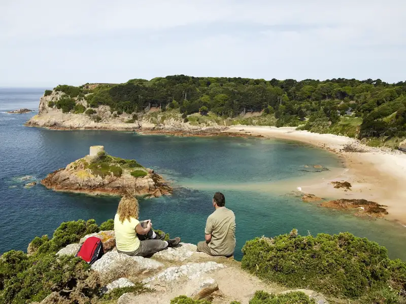 Zwei Reisende einer Studienreise genießen von einer Klippe den Ausblick auf die malerische Portelet Bay auf Jersey.