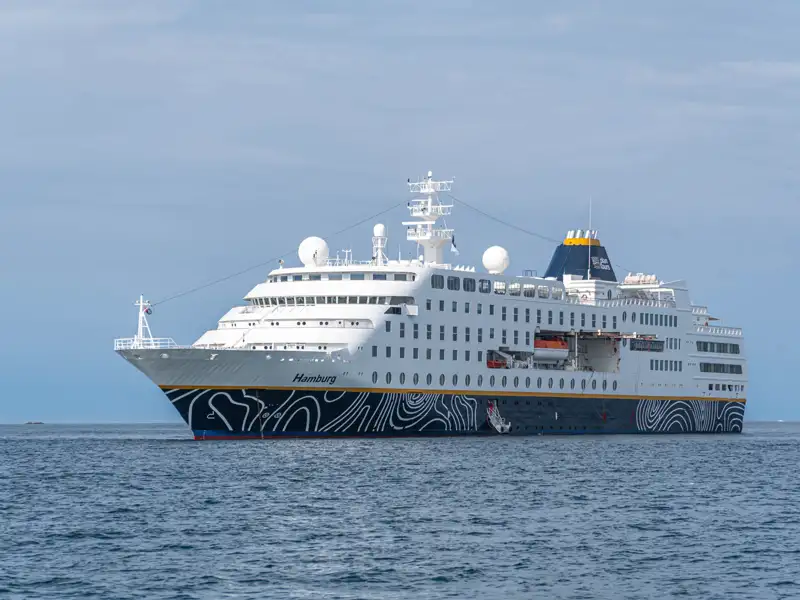 Das weiße Kreuzfahrtschiff MS Hamburg mit seinem markant verzierten Rumpf gleitet bei Tageslicht über das ruhige, blaue Meer.