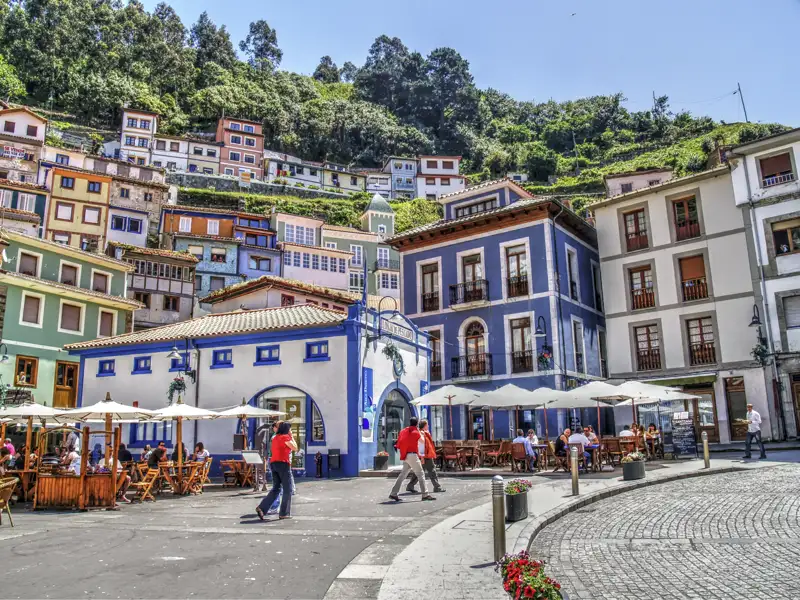 Sonnige Plaza im Fischerdorf Cudillero in Asturien mit bunten Häusern am Hang und belebten Terrassen von Cafés, ein Hingucker auf unserer Kulturreise mit Studiosus.