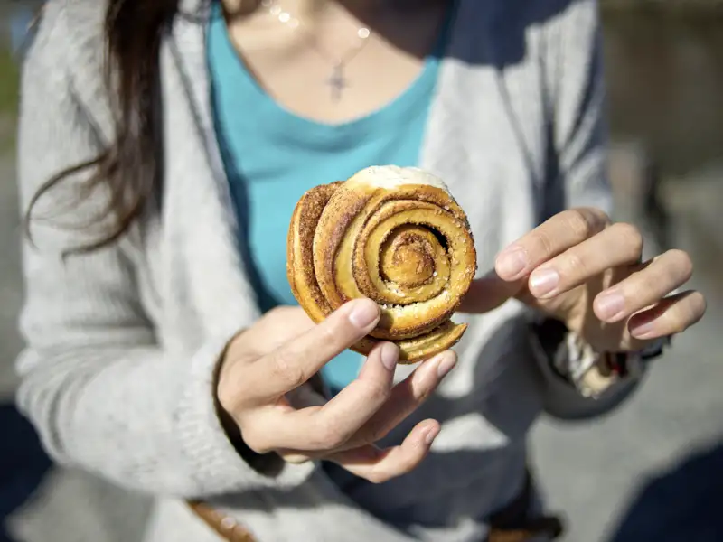 Nahaufnahme der Hände einer Frau, die eine typisch norwegische Zimtschnecke, eine sogenannte Kanelsnurr, hält.