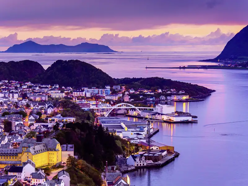 Abendlicher Blick auf die erleuchtete Jugendstilstadt Alesund in Norwegen, umgeben vom Meer.