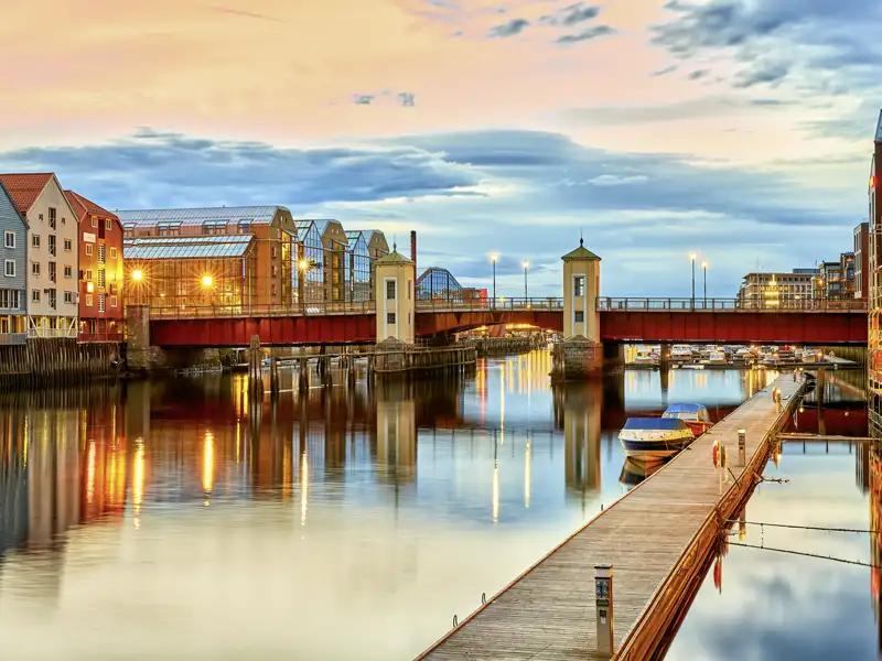 Stimmungsvolle Abenddämmerung in Trondheim: Bunte Lagerhäuser und die Bakke-Brücke spiegeln sich im ruhigen Fluss Nidelven.