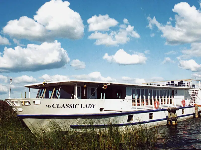 Das Passagierschiff MS Classic Lady ankert an einem sonnigen Tag am schilfbewachsenen Ufer eines Sees in der Masurischen Seenplatte Polens.