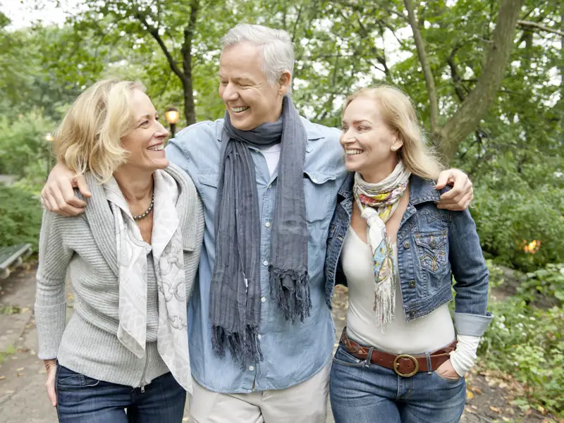 Drei gut gelaunte Teilnehmer einer Gruppenreise mit Studiosus spazieren Arm in Arm durch den Central Park in New York und lachen miteinander.