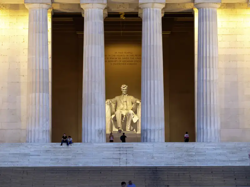 Monumentale, sitzende Statue von Abraham Lincoln im abends beleuchteten Lincoln Memorial in Washington mit Besuchern auf den Stufen, ein toller Anblick, den wir auf unserer Rundreise mit Studiosus in die USA bewundern.