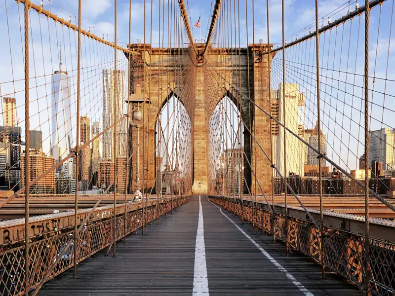 Der leere Fußgängerweg der Brooklyn Bridge in New York City führt im warmen Licht auf die Skyline von Manhattan zu, ein Highlight, über diese auf unserer Gruppenreise mit Studiosus zu spazieren.