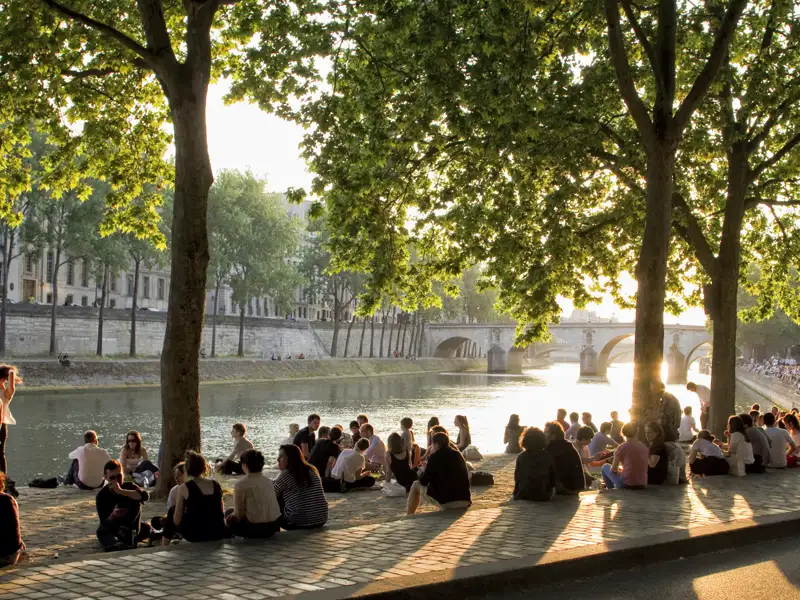 Paris, eine Stadt der Flaneure und Genießer! Auf unserer Städtereise zeigt uns die Studiosus-Reiseleiterin bzw. der Studiosus-Reiseleiter jede Menge bekannter und auch unbekannter romantischer Winkel in Paris. An einem schönen Sommerabend versammeln sich viele Pariser und Pariserinnen an den Ufern der Seine, um den Sonnenuntergang und die Stimmung in der Stadt zu genießen.