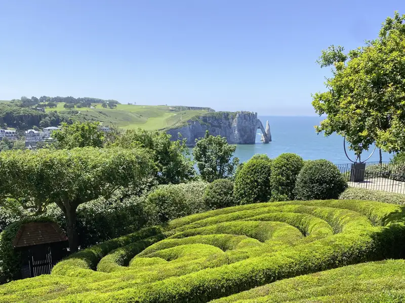 Kunstvoll geschnittene Hecken im Garten von Étretat mit Blick auf die berühmte Felsformation Porte d'Aval an der Küste der Normandie, welche wir bei unserer Rundreise mit Studiosus bewundern können.