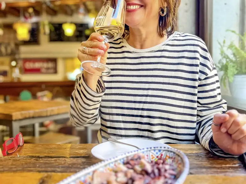 Lächelnde Frau in einem Restaurant, die während ihrer Studienreise ein Glas Weißwein und lokale Spezialitäten genießt.