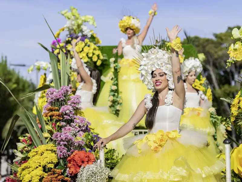 Auf unserer Gruppenreise mit Studiosus bewundern wir Tänzerinnen in aufwendigen gelben Blumenkostümen winken von einem prächtigen Festwagen beim Blumenfest in Funchal.