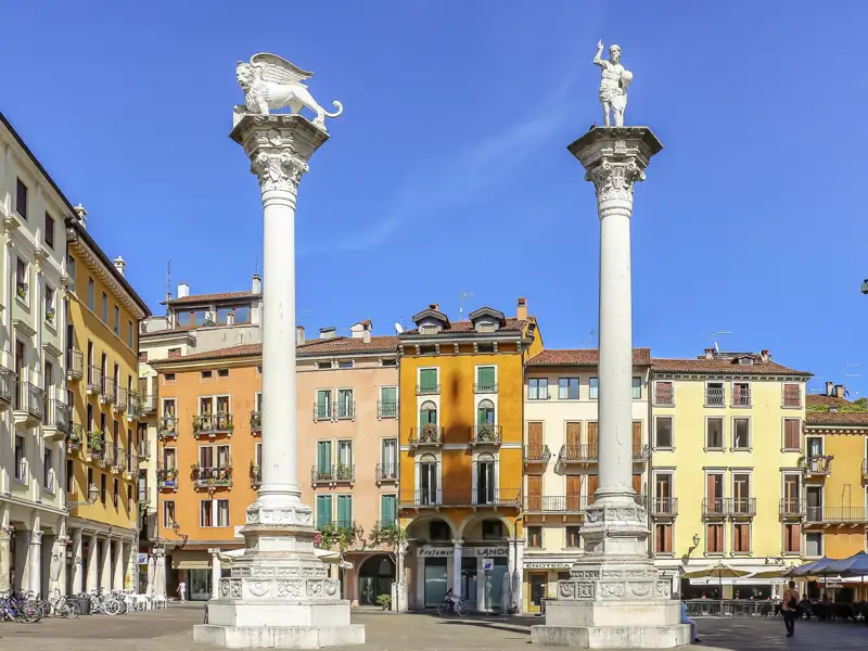 Auf unserer Gruppenreise mit Studiosus nach Italien sehen wir die Säulen mit dem Markuslöwen und der Erlöserstatue auf der Piazza dei Signori in Vicenza vor bunten Fassaden.