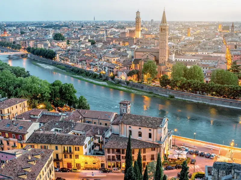 Weitblick über die historische Altstadt von Verona in der Abenddämmerung, entlang des Flusses Etsch mit beleuchteten Gassen, ein Highlight jeder Studiosus Rundreise nach Italien.