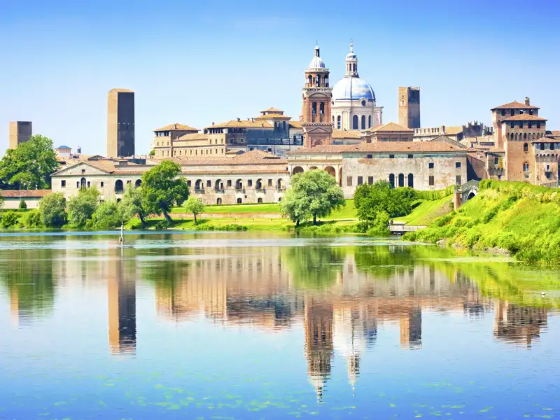 Historische Altstadt von Mantua mit dem Palazzo Ducale, die sich an einem sonnigen Tag im ruhigen Fluss Mincio spiegelt, ein Highlight jeder Studiosus Gruppenreise nach Italien.