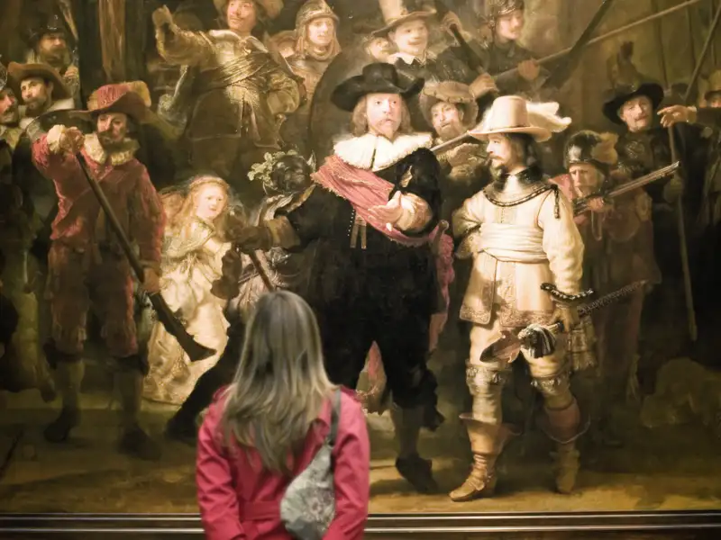 Teilnehmerin einer Studiosus Studienreise betrachtet Rembrandts berühmtes Gemälde 'Die Nachtwache' im Rijksmuseum Amsterdam.