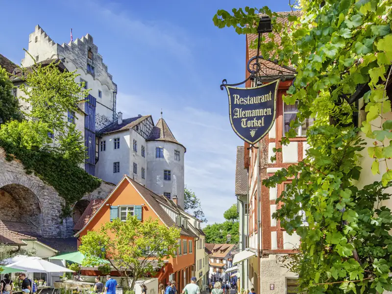 Blick durch eine malerische Gasse in Meersburg auf die historische Burg, Fachwerkhäuser und das Restaurant Alemannen Torkel, ein Highlight unserer Studiosus Gruppenreise an den Bodensee.