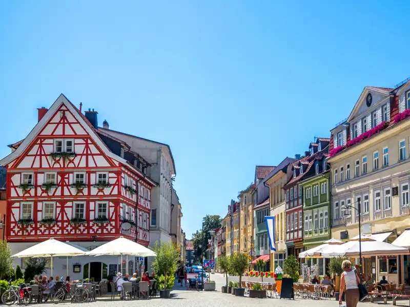 Auf unserer Gruppenreise mit Studiosus werfen wir einen Blick auf den belebten Herderplatz in Weimar, ein Höhepunkt der Städtereise, mit seinem markanten roten Fachwerkhaus und den gemütlichen Außenterrassen der Cafés bei blauem Himmel.