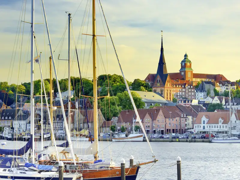 Segelboote im Flensburger Hafen vor den Giebelhäusern der Altstadt, über die der Turm der Marienkirche ragt, ein Highlight unserer Gruppenreise nach Norddeutschland.