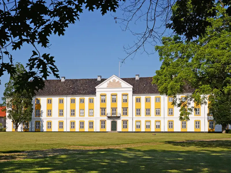 Die prachtvolle, weiße Fassade des Barockschloss Augustenborg in Dänemark, gesehen über den Schlosspark bei blauem Himmel, ein toller Ausflug auf unserer Gruppenreise mit Studiosus.
