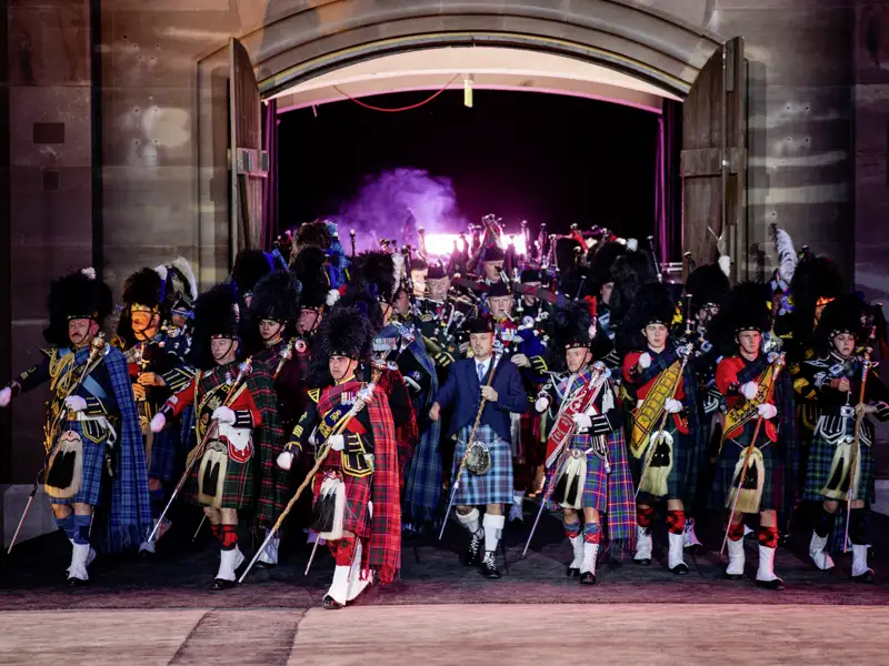 Musiker in schottischen Kilts marschieren nachts beim Basel Tattoo aus einem Tor der historischen Kaserne, ein absoltues Highlight auf unserer Eventreise nach Basel.