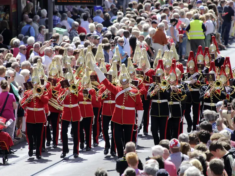 Ein Militärorchester in roten Uniformen marschiert während der Eventreise zum Basel Tattoo durch eine von Zuschauern gesäumte Straße, ein Highlight der Studiosus Eventreise nach Basel.
