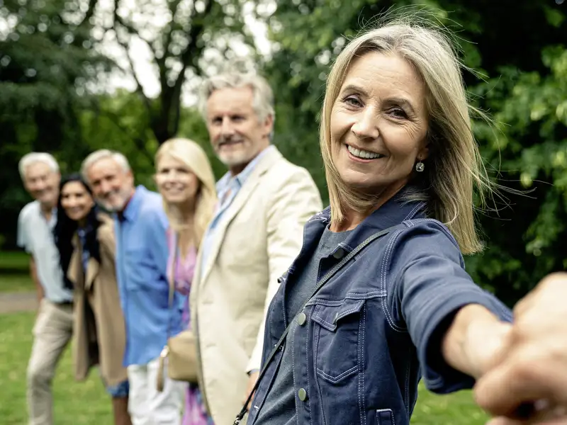 Eine lächelnde Frau nimmt den Betrachter bei der Hand und führt ihn auf einer geführten Gruppenreise durch einen Park im Sommer.