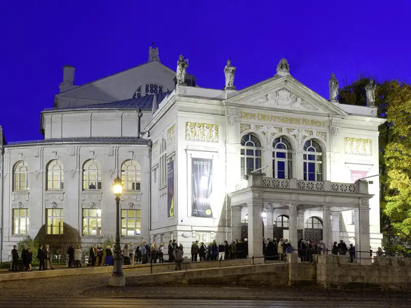 Elegant gekleidete Gäste einer Studiosus Eventreise versammeln sich am Abend vor dem beleuchteten Prinzregententheater in München.